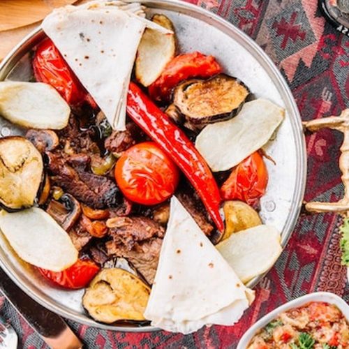 מזה קפריסאי אותנטי עם בשר צלוי, פיתה, עגבניות וסלטים על שולחן טברנה כפרית ליד פרוטארס